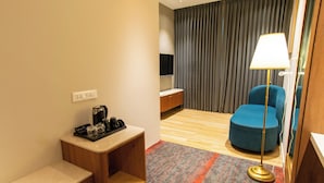 A hotel room with a wooden desk, a blue armchair, a standing lamp, and a TV mounted on the wall. - Hotel Sing 65 (Bengaluru)
