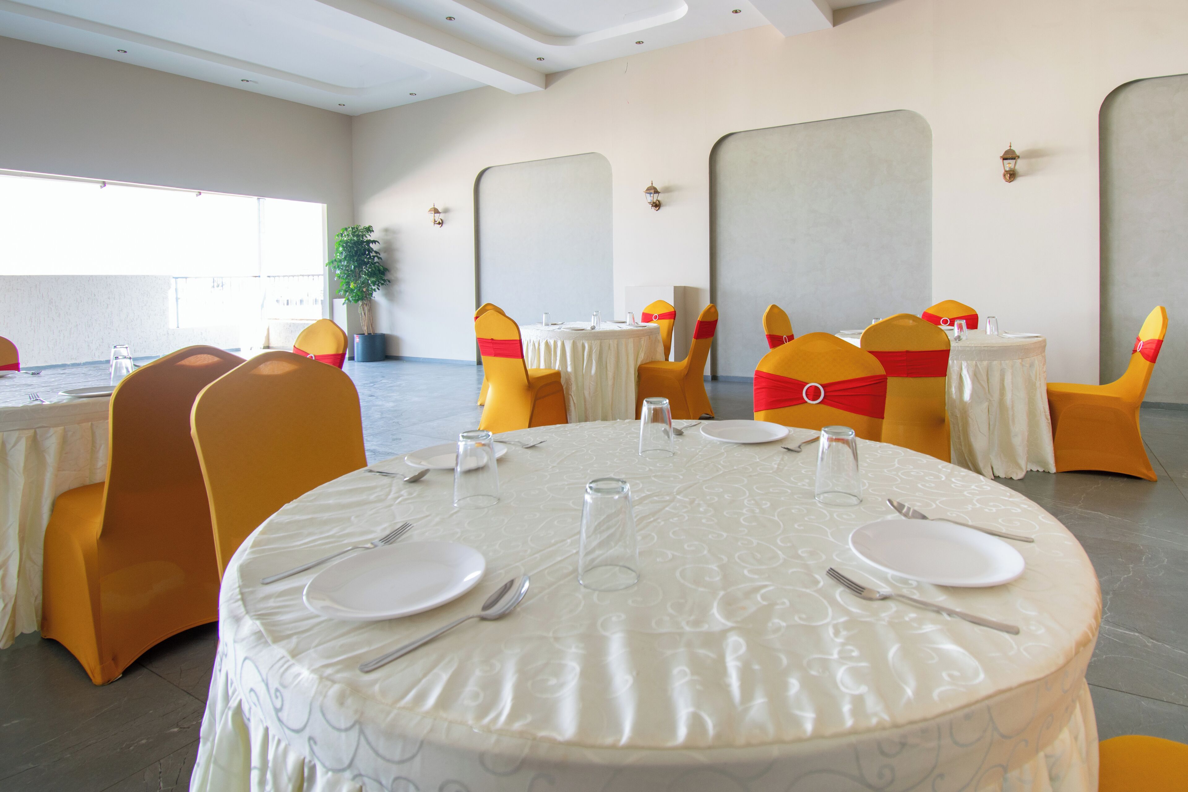 Un comedor con mesas redondas, sillas amarillas y manteles blancos.
