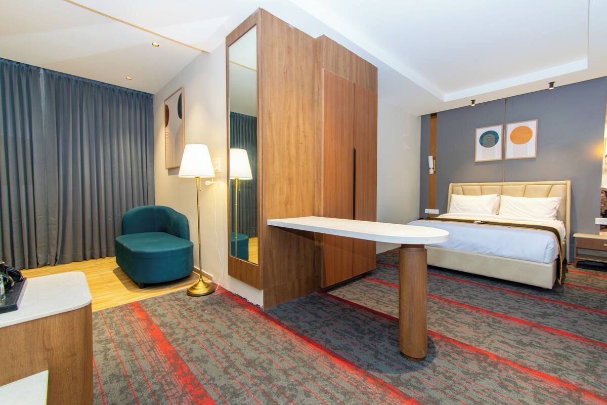 A hotel room with a bed, a desk, a chair, a mirror, and a carpeted floor.