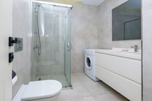 A modern bathroom with a glass-enclosed shower, a washing machine, and a white vanity. - lUX RESIDENCE IN HIGH FLOOR (Istanbul)
