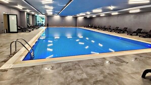 Ein Hallenbad mit Fliesenboden, einer Poolleiter und Liegestühlen entlang der Wände.