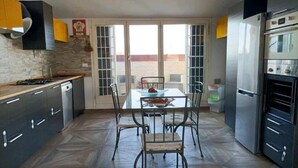 Eine moderne Küche mit Esstisch und Stühlen, einem großen Fenster und einem Kühlschrank.