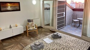 Ein Hotelzimmer mit Bett, Stuhl, kleinem Tisch, Kleiderständer und einem Balkon mit Blick auf die Stadt.