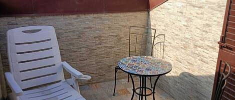 Un pequeño patio al aire libre con dos sillones blancos, una mesa redonda pequeña y un muro de piedra.