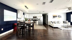 A modern kitchen with white cabinets, stainless steel appliances, and a dining area with a wooden table and chairs. - Home Close to Clearwater Beach (Largo)