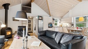 Een gezellige woonkamer met een open haard, een zwarte leren bank, een houten bijzettafeltje en een eethoek met een tafel en stoelen.