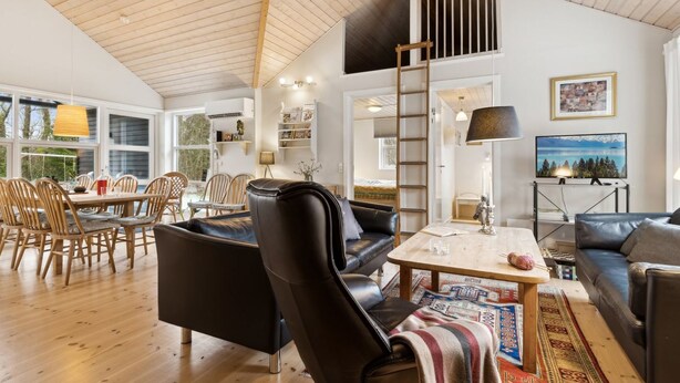 Een ruime woonkamer met een hoge plafond, houten vloer, een eethoek, een bank, een salontafel en een televisie.