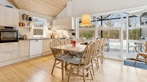 Een ruime keuken met houten kastjes, een eethoek met een grote tafel en stoelen, en grote ramen die zorgen voor natuurlijk licht.