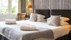 Ein Hotelzimmer mit einem großen Bett, zahlreichen Kissen, einem Nachttisch mit Lampe und Blick auf Grün.