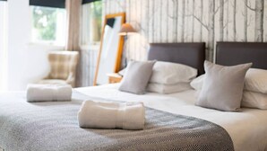 A neatly made bed with pillows and a folded towel, a bedside table with a lamp, and a window with curtains.