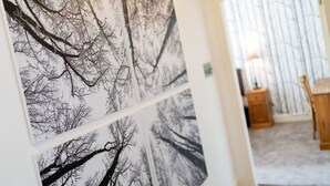 A hallway with a series of black and white tree photographs on the wall, leading to a room with a wooden table and a lamp.