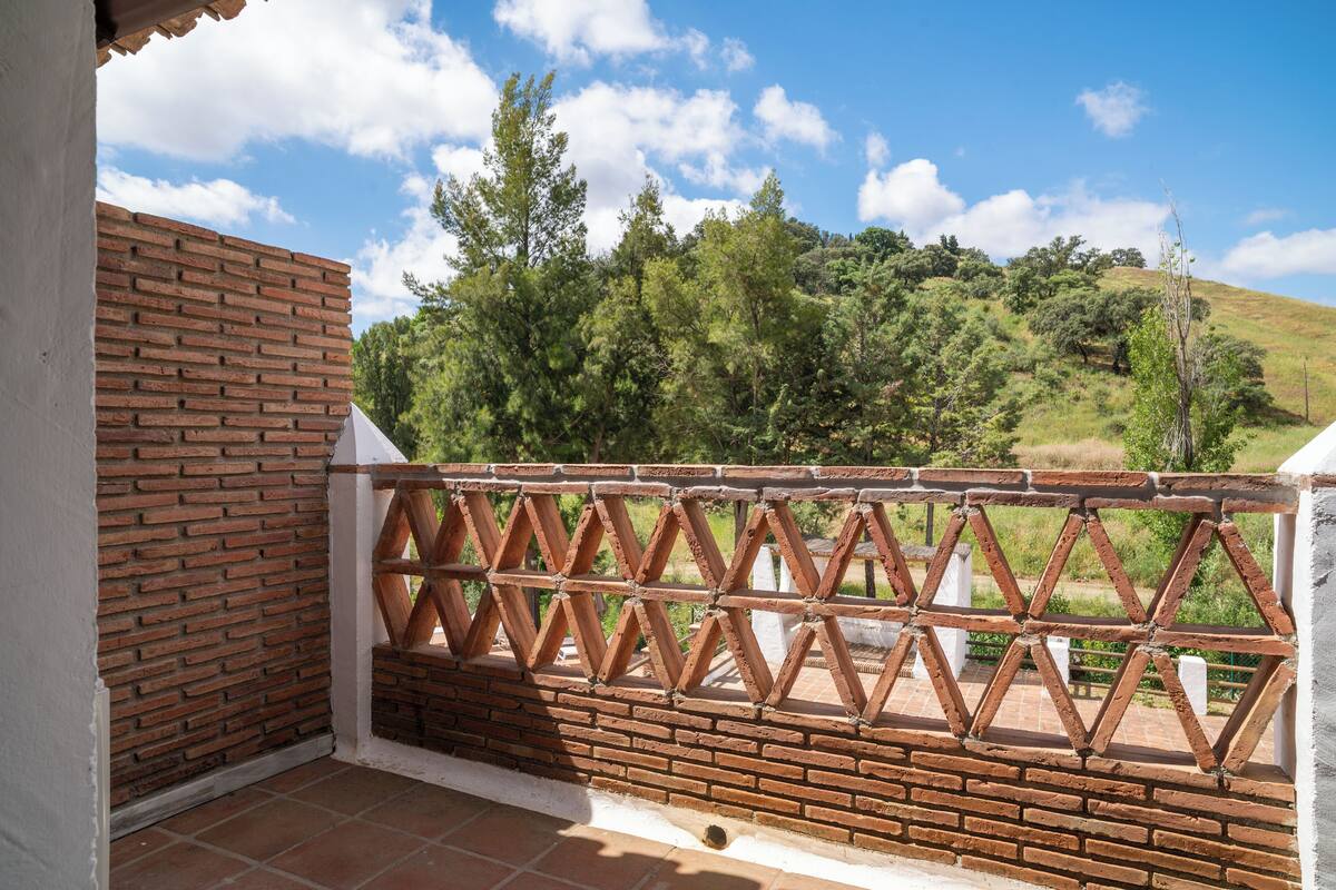 Un balcon avec un mur en briques et une clôture en treillis, donnant sur une colline boisée.