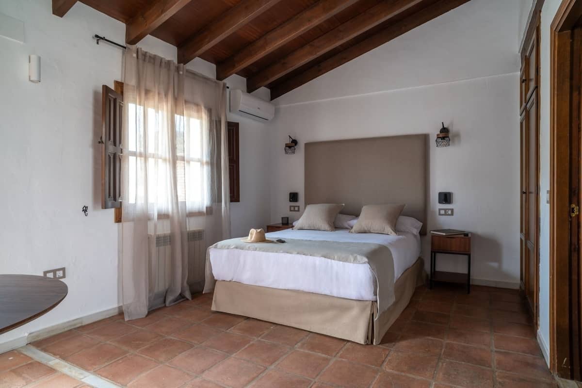 Une chambre à coucher avec un grand lit, un plafond en bois, une table de chevet et une fenêtre avec des rideaux.