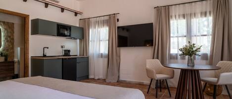 Une chambre d’hôtel comprenant un lit, une table à manger avec des chaises, un coin cuisine avec un four à micro-ondes et un téléviseur fixé au mur.