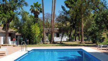 Una piscina con agua cristalina azul, rodeada de árboles y un edificio al fondo.