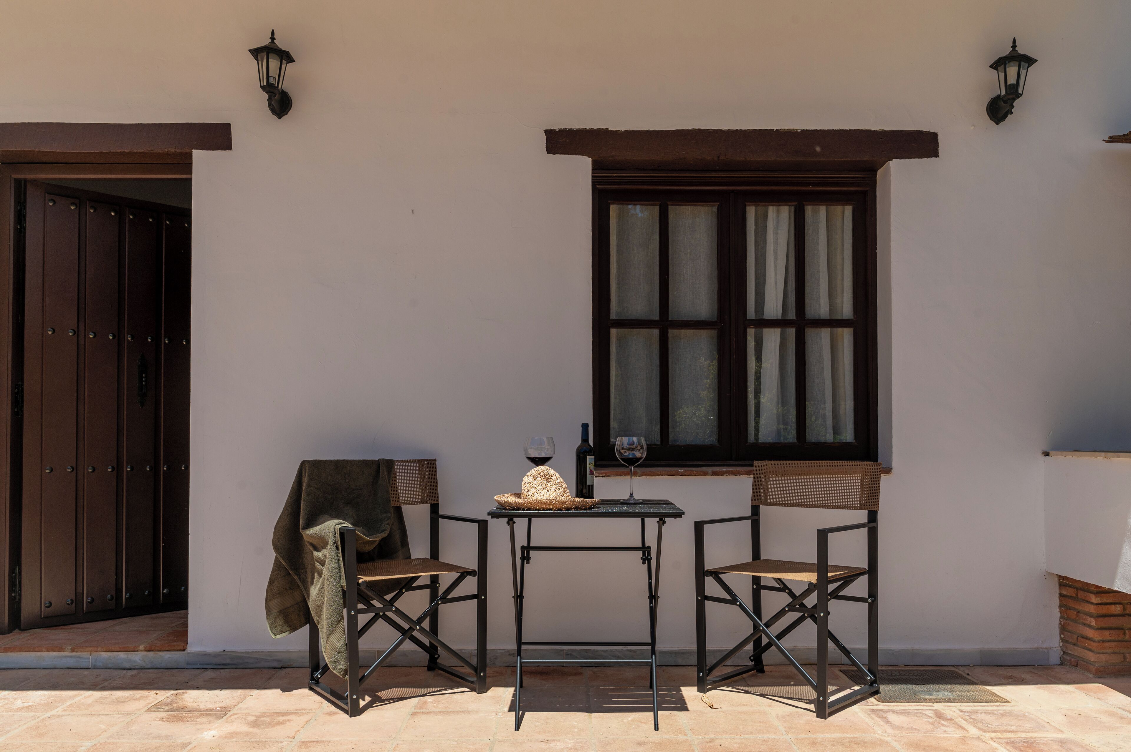 Un patio con dos sillas, una mesa y un ventanal con cortinas.