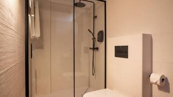 Un baño moderno con ducha de vidrio, inodoro y dispensador de papel higiénico en la pared.