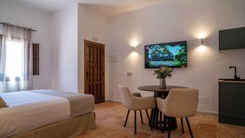 Habitación de hotel con una cama, un televisor montado en la pared, una pequeña mesa de comedor con sillas y una puerta de madera.