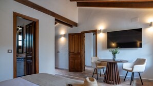 Una habitación de hotel con una cama, una mesa redonda con sillas, un televisor montado en la pared y puertas de madera.