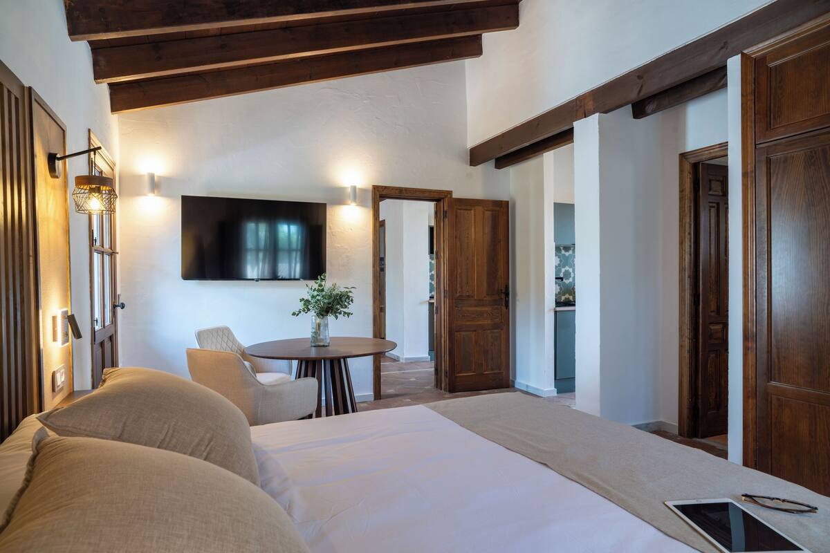 Une chambre d’hôtel avec un lit, une table ronde ornée d’un vase, une chaise et un téléviseur fixé au mur.