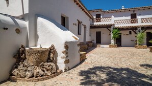 Un patio con paredes blancas, techo de tejas y escalones de piedra que conducen a una puerta de madera.