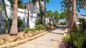 Una calle adoquinada bordeada de edificios blancos, palmeras y un muro de piedra con flores coloridas.