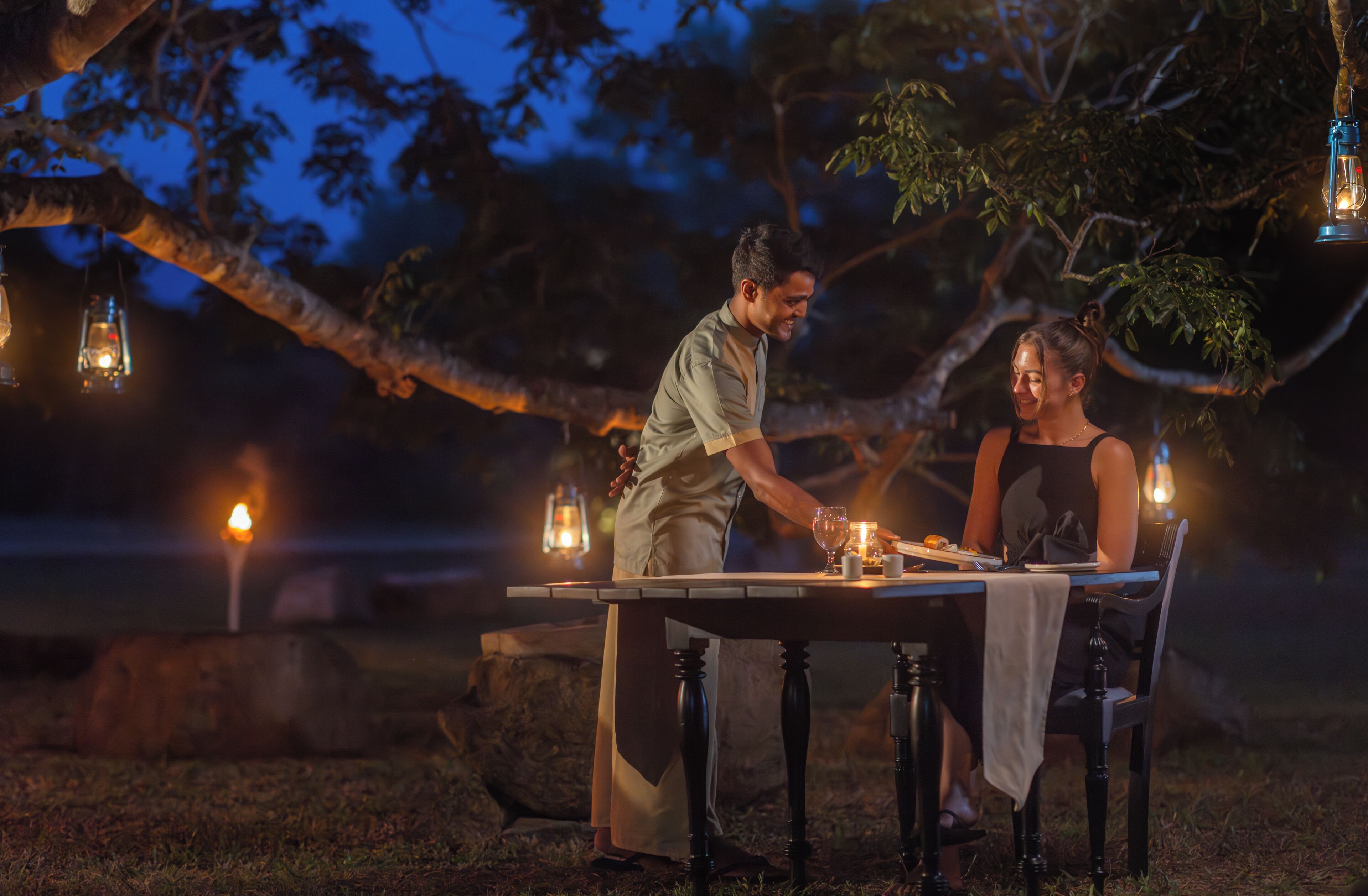 An outdoor dining table set up under a tree with lanterns.