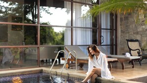 A pool area with a glass wall, lounge chairs, and a stone wall. - Ayugiri Ayurveda Wellness Resort  (Sigiriya)