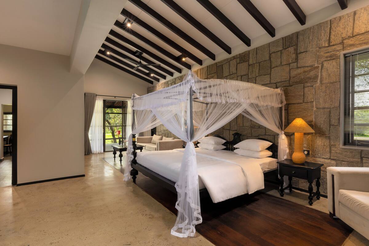 Un dormitorio con cama con dosel, pared de piedra y mesita de noche con lámpara.
