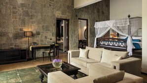 A spacious living area with a stone wall, a sofa, a coffee table, and a bed with a canopy. - Ayugiri Ayurveda Wellness Resort  (Sigiriya)