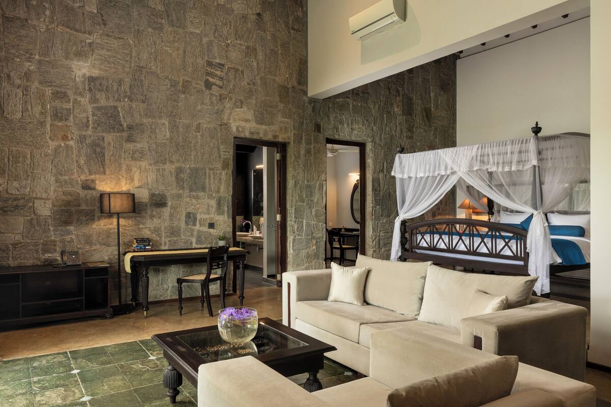 Amplia sala de estar con pared de piedra, un sofá, una mesa de centro y una cama con dosel.