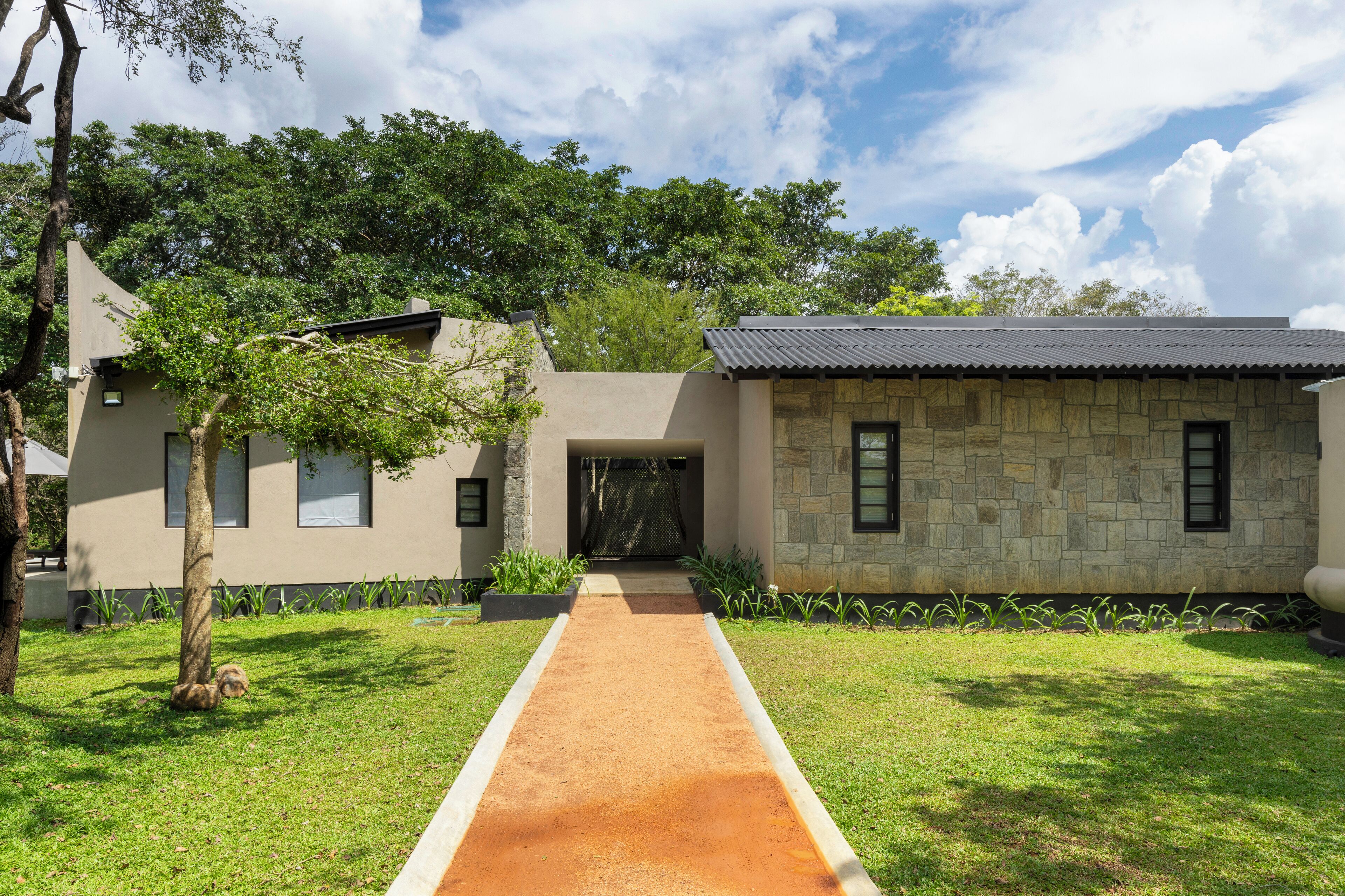 A modern house with a stone facade, a paved pathway, and a well-maintained lawn.