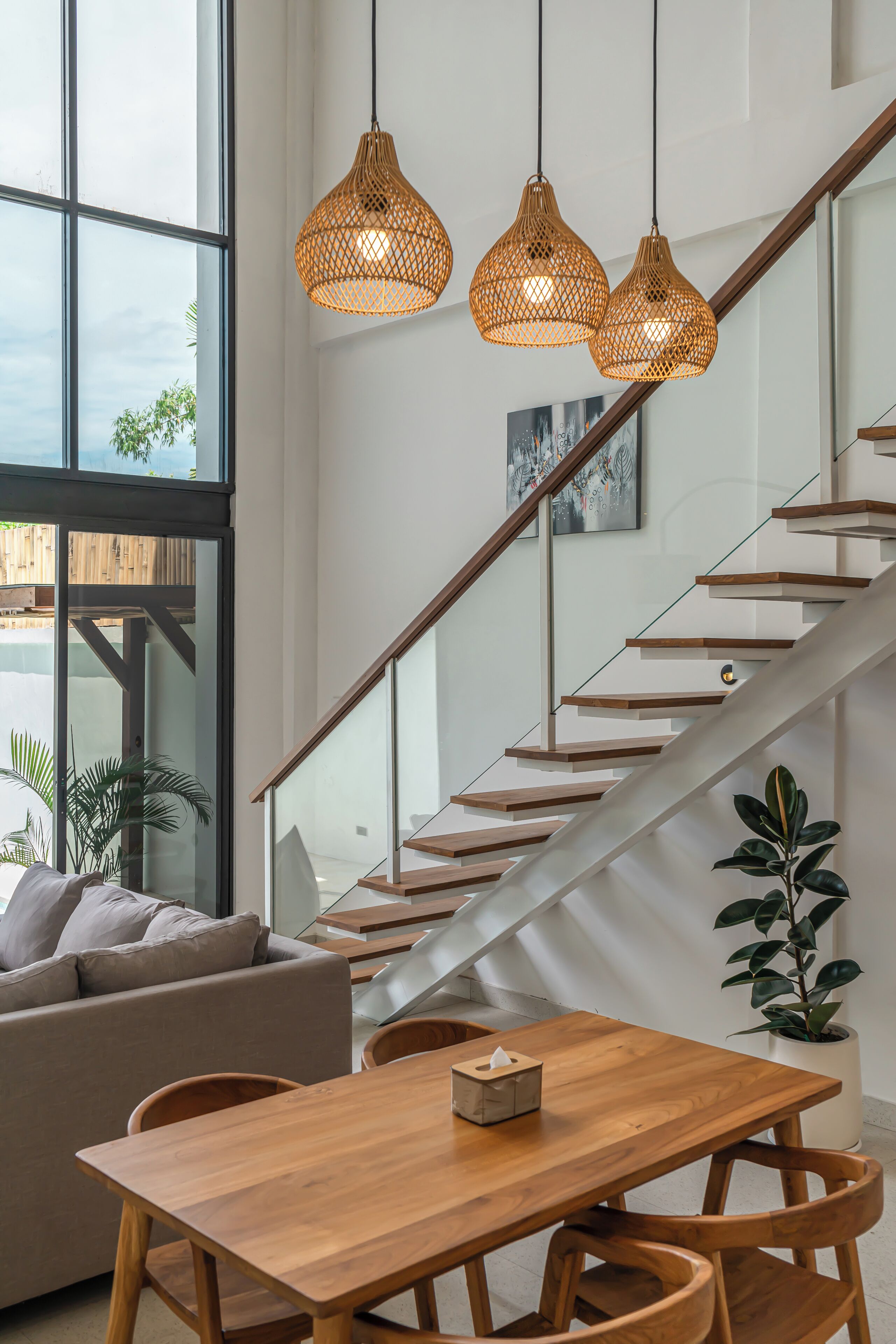 Ein modernes Interieur mit einem Holzesstisch, einer Couch und einer Treppe mit Glastrennwand.