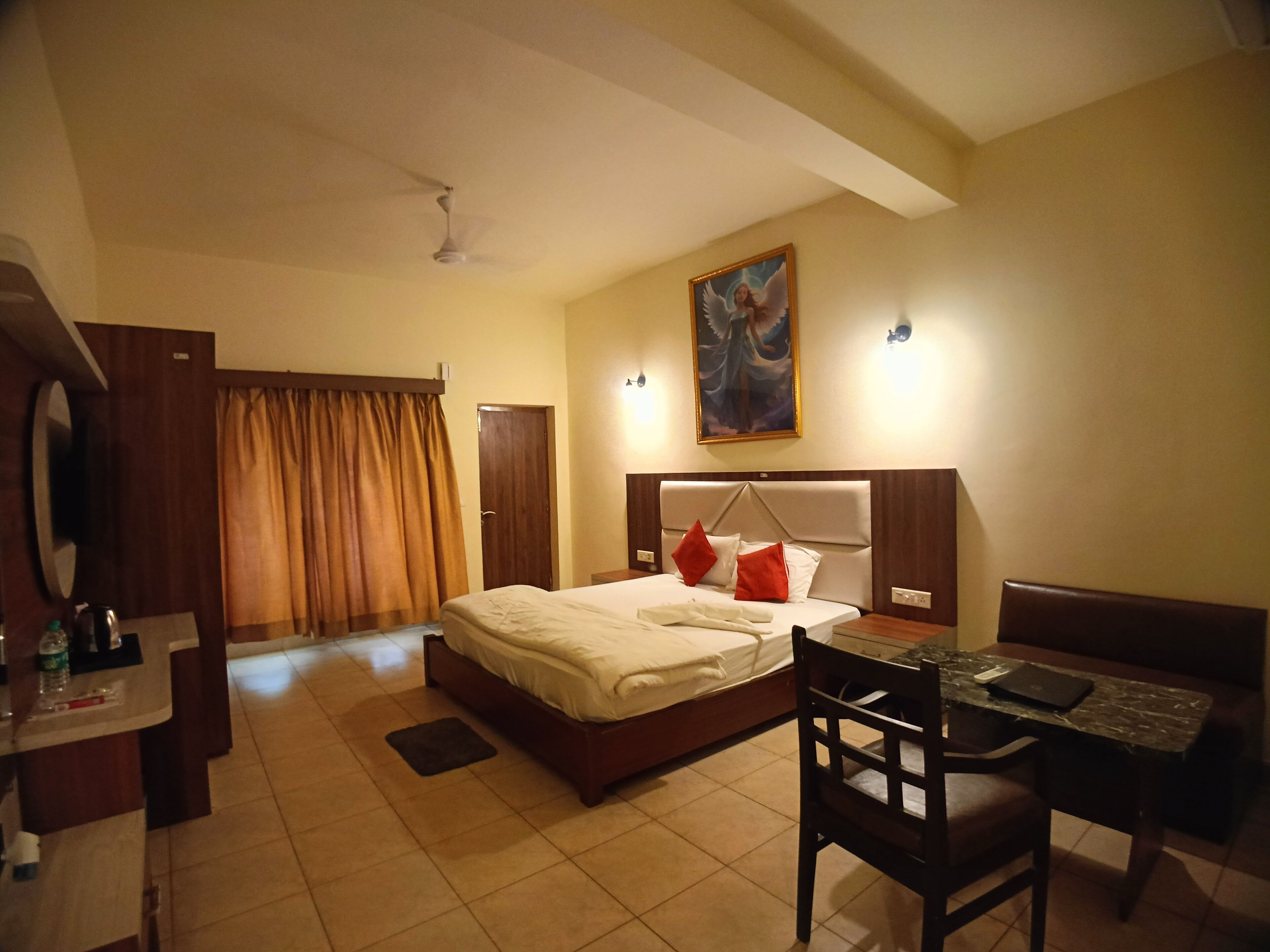 Habitación de hotel con cama, escritorio, silla, mesa, ventilador de techo y un cuadro en la pared.