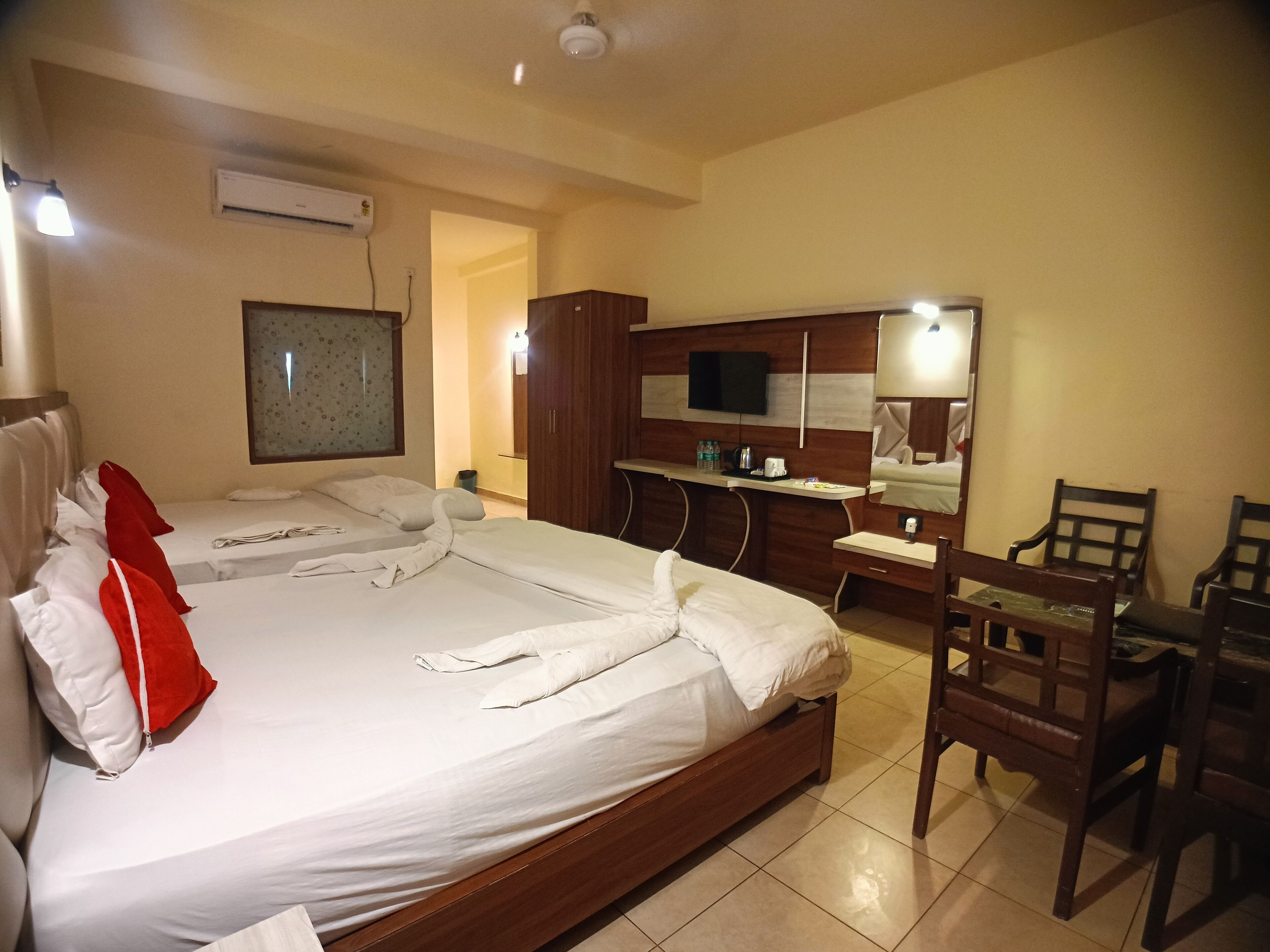 A hotel room with two beds, a desk, a mirror, and a TV.