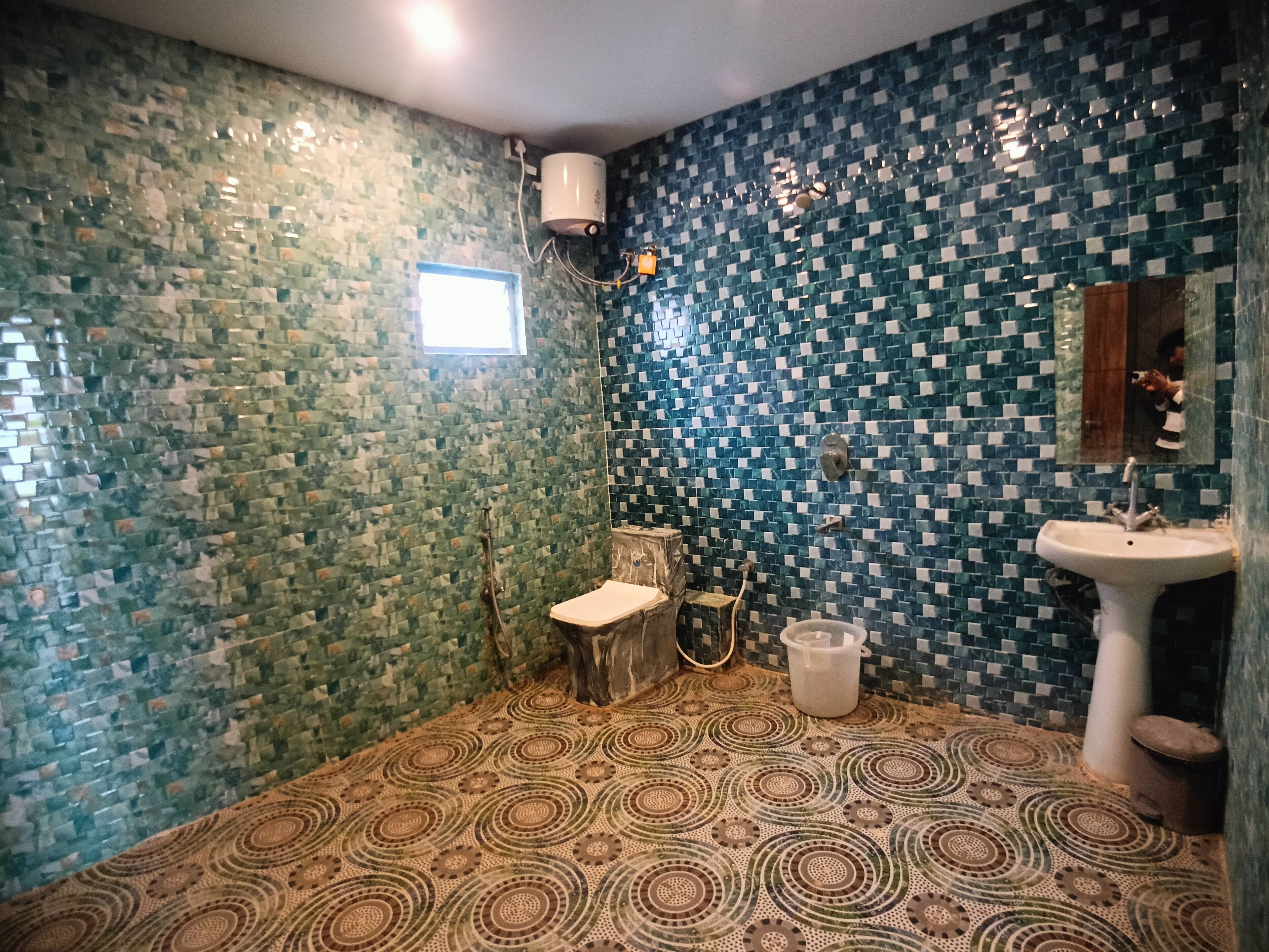 A bathroom with mosaic tile walls, a patterned floor, a toilet, a sink, and a shower area.