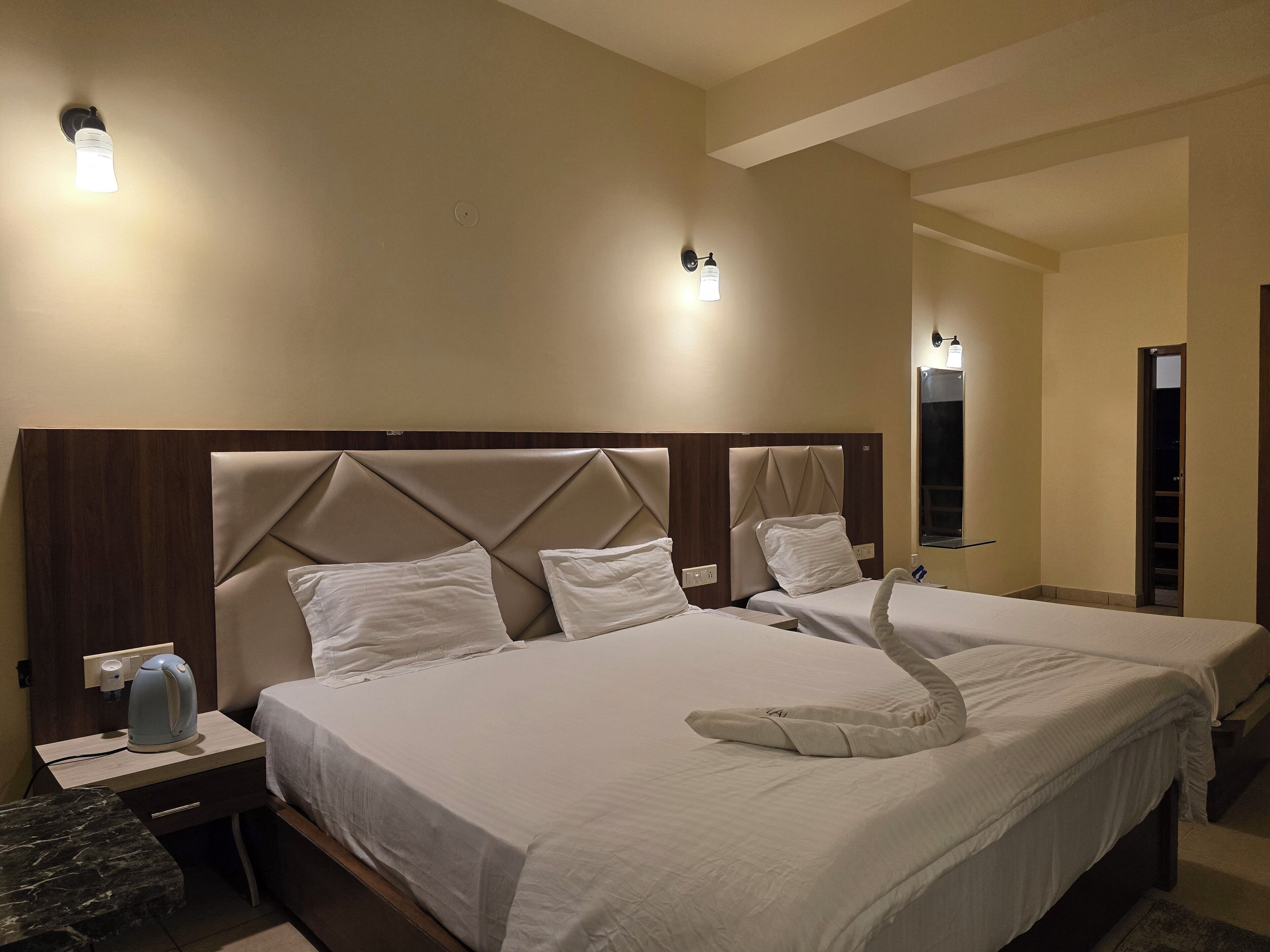Habitación de hotel con una cama grande, una mesita de noche con hervidor y dos lámparas fijadas a la pared.