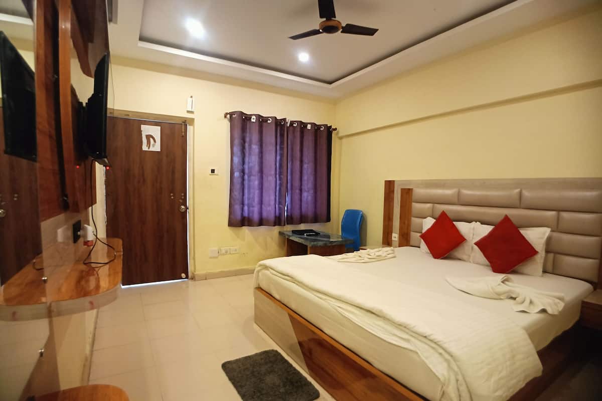 A bedroom with a bed, a desk, a chair, a ceiling fan, and a window with curtains.