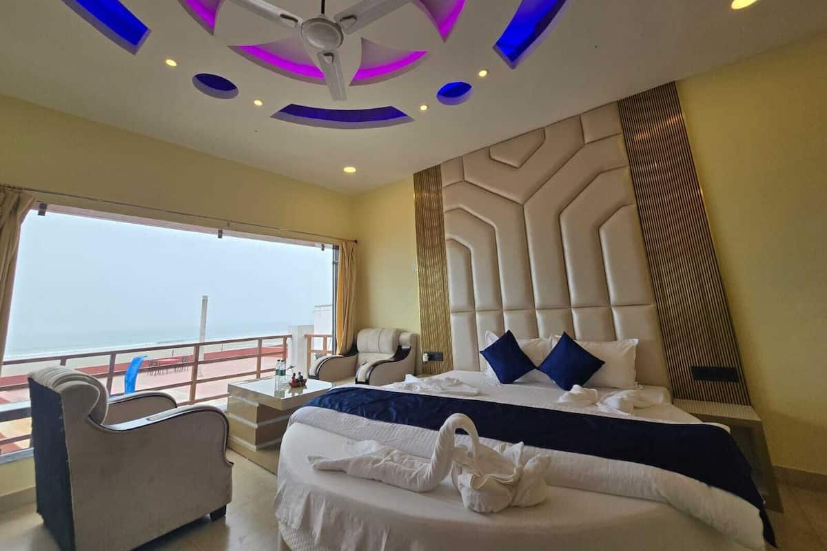 A hotel room with a large bed, a ceiling fan, a view of the sea, and a balcony.