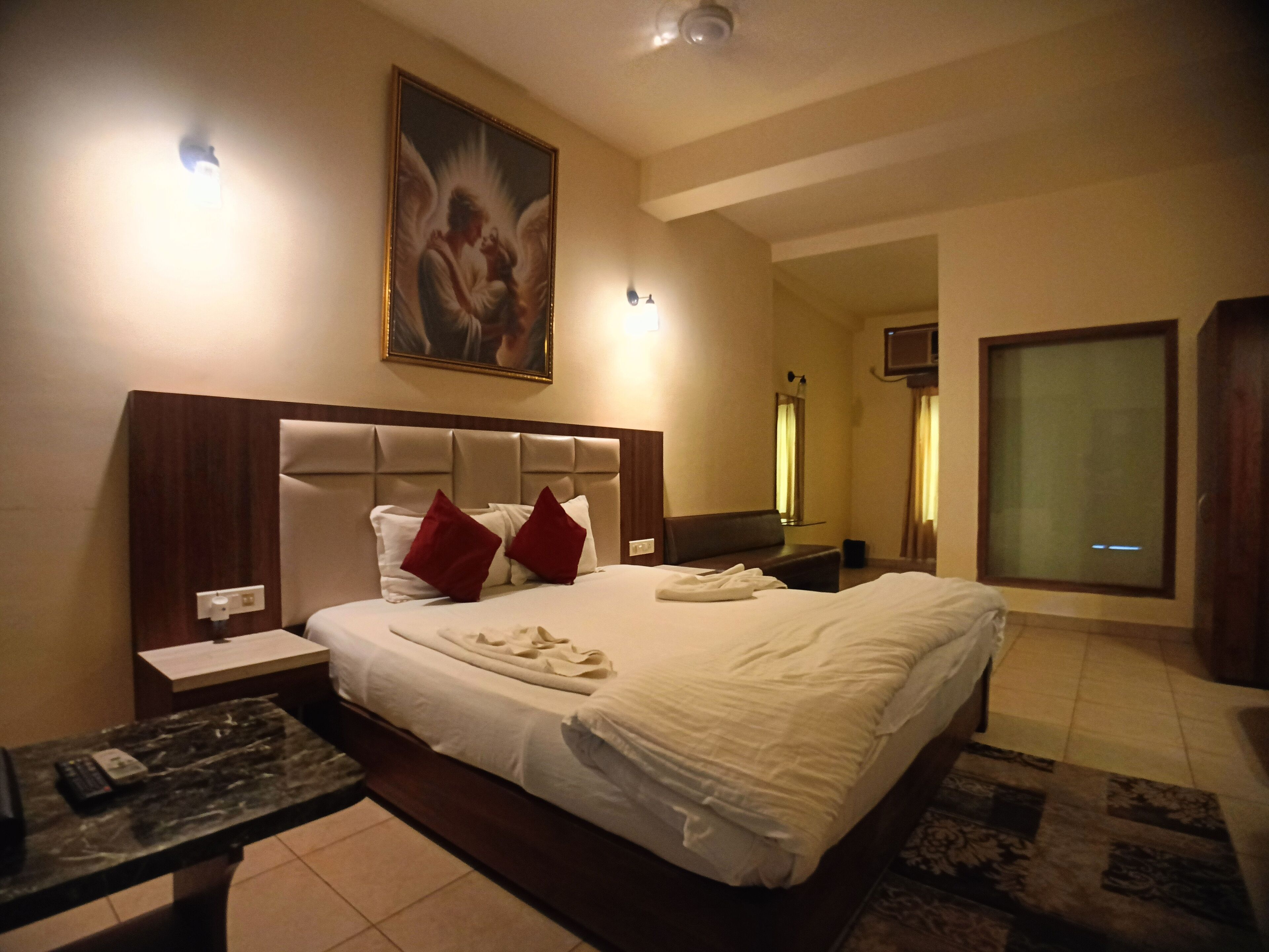 Una habitación de hotel con una cama grande, un cabecero, un cuadro en la pared, un escritorio y un espejo.