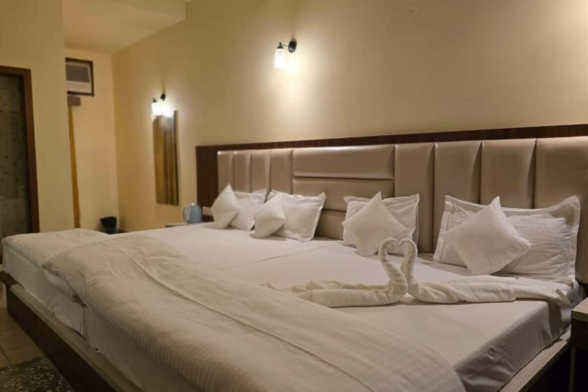 A neatly made bed with a swan-shaped towel arrangement, a headboard with built-in lighting, and a bedside table with a lamp.