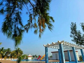 A pool area with a covered seating area, palm trees, and a slide.