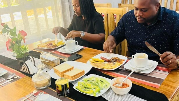 A dining table set with various dishes, utensils, and a vase with flowers. - Sunset Inn Arusha (Arusha)