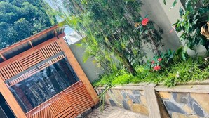 A wooden structure with a slatted design, a stone retaining wall, and lush greenery with red flowers. - Sunset Inn Arusha (Arusha)