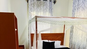 A bedroom with a wooden four-poster bed, a canopy, and a ceiling fan. - Sunset Inn Arusha (Arusha)