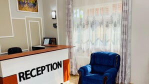 A reception area with a reception desk labeled "RECEPTION," a blue armchair, and a blue sofa. - Sunset Inn Arusha (Arusha)
