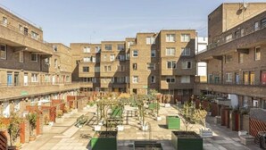 Une cour intérieure bordée de plusieurs immeubles d’appartements, avec des espaces de détente en plein air et des plantes en pot.