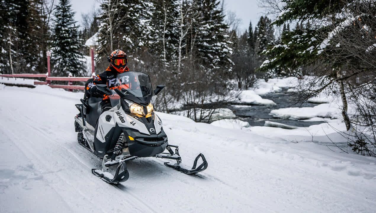 A snowmobile on a snowy path with trees in the background.