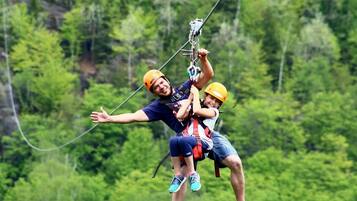 Zwei Personen mit Sicherheitsausrüstung beim Ziplining inmitten eines bewaldeten Gebiets.