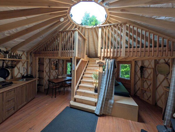 Una cabaña de madera con un dormitorio en el altillo, una cocina con armarios de madera y un comedor.